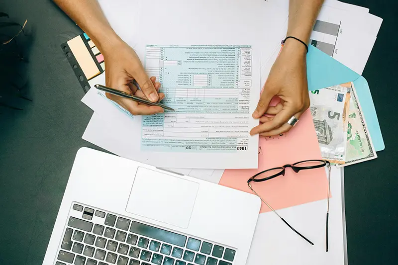 top-down view of a person filling out a tax form on a desk with a laptop and glasses
