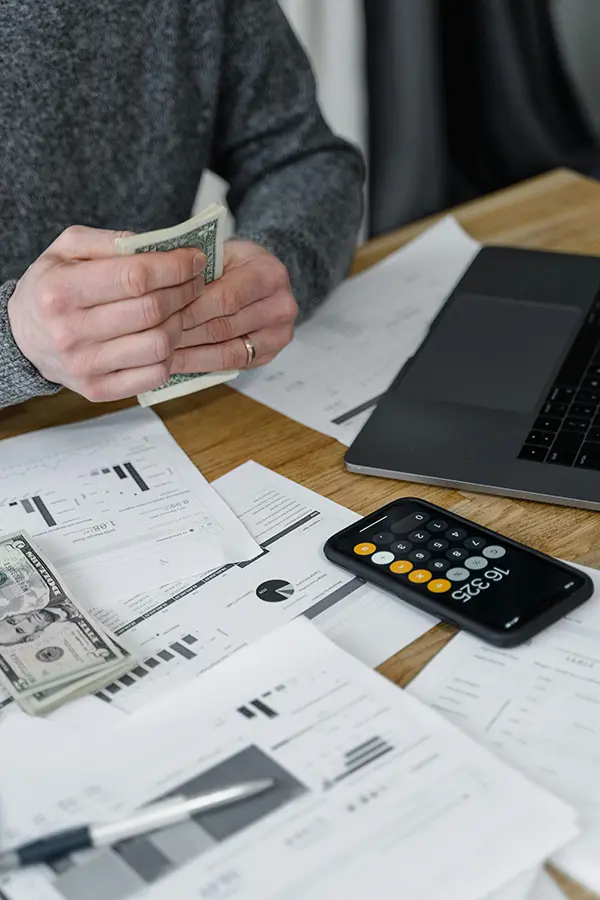 Person counting money at a desk with paper forms and a laptop